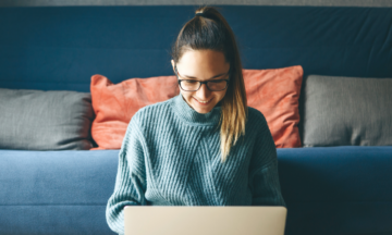 A person in a blue sweater looking at a laptop.