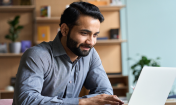 A smiling man working on a laptop.